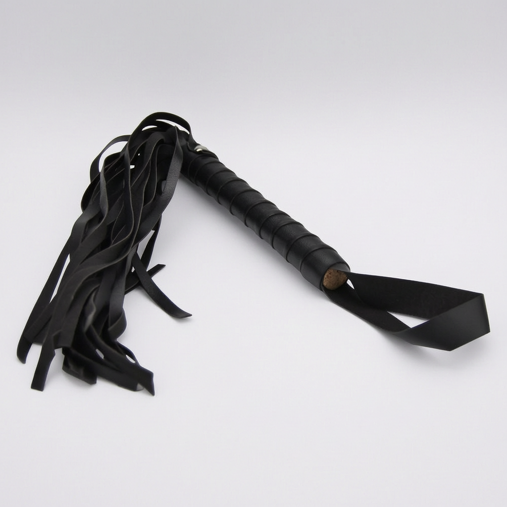 Black leather flogger whip with a textured grip handle and a long tail of hanging straps, shown on a light grey background.