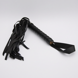 Black leather flogger whip with a textured grip handle and a long tail of hanging straps, shown on a light grey background.